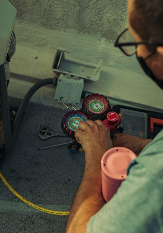 Technician using a manifold gauge to check refrigerant pressure on a cooling unit