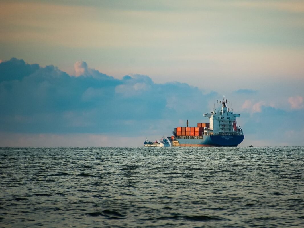 Container ship loaded with cargo sailing near port at dusk