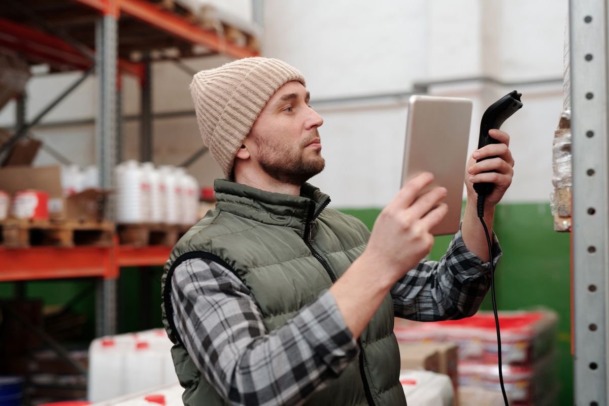 Warehouse worker with handheld scanner and tablet checking stock on shelving