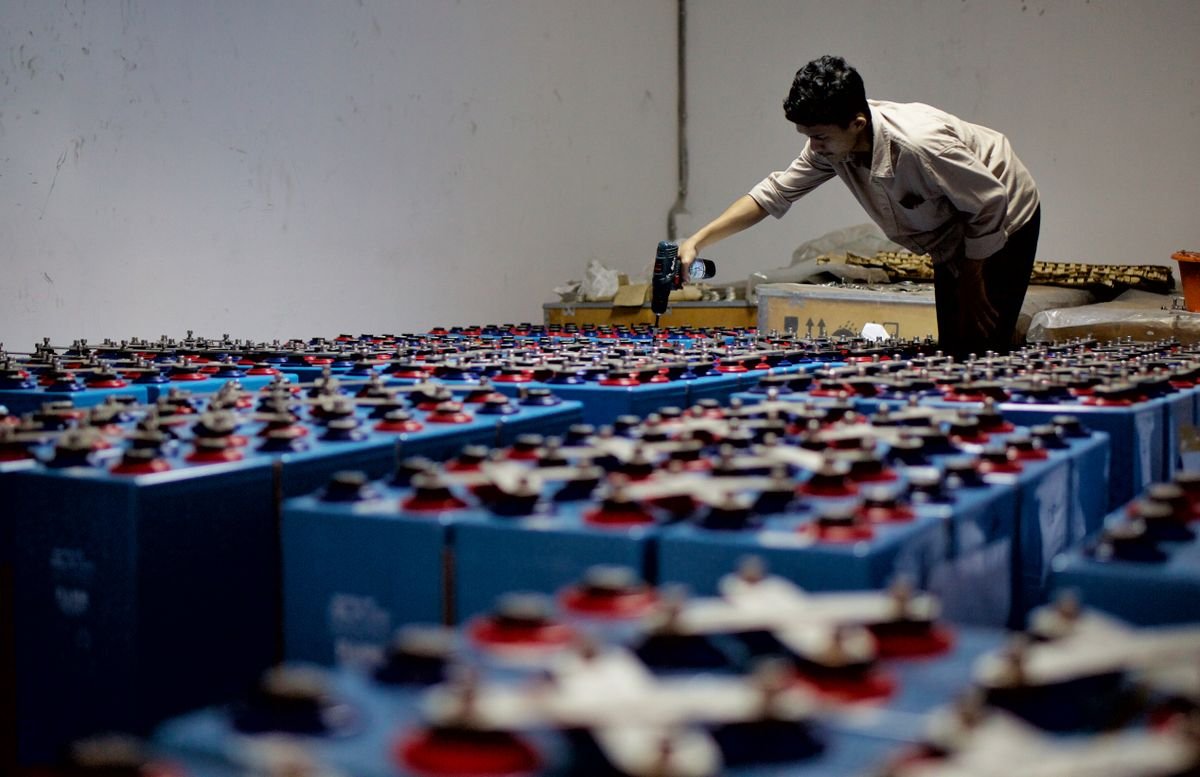 Worker inspecting rows of industrial storage batteries in a facility