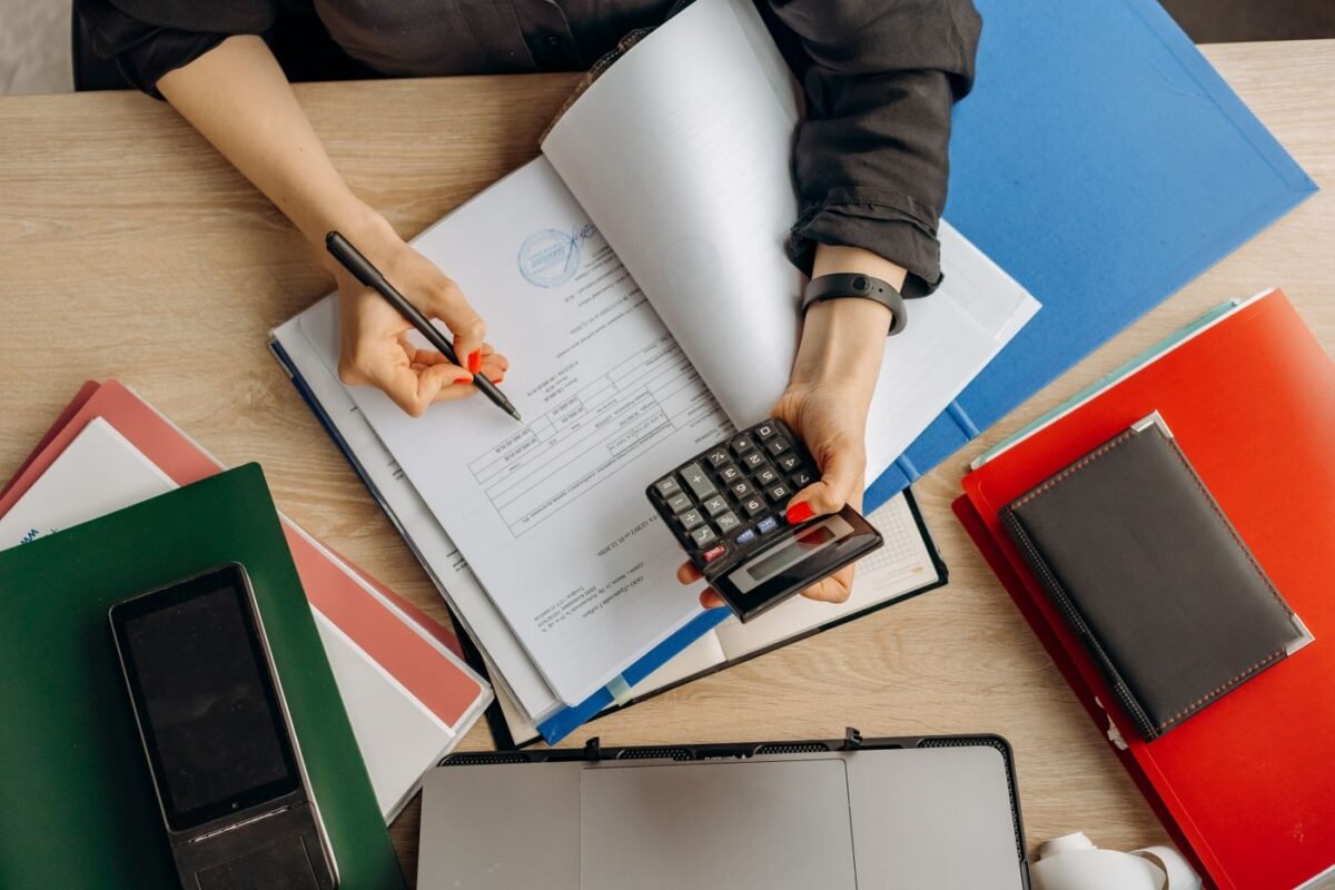 Accountant using a calculator on a stamped invoice with folders