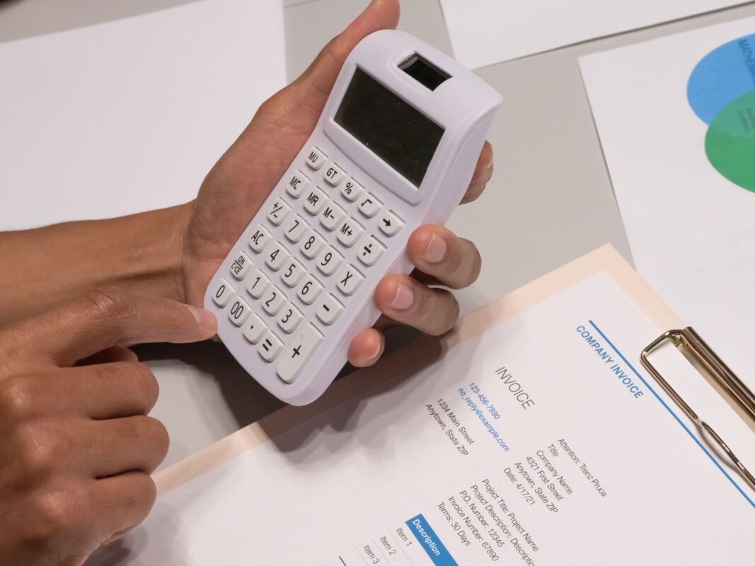 Hands using a calculator next to a company invoice to work out a payment plan