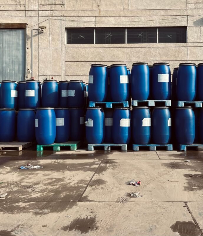 Rows of blue industrial chemical drums stacked on pallets outside a warehouse facility