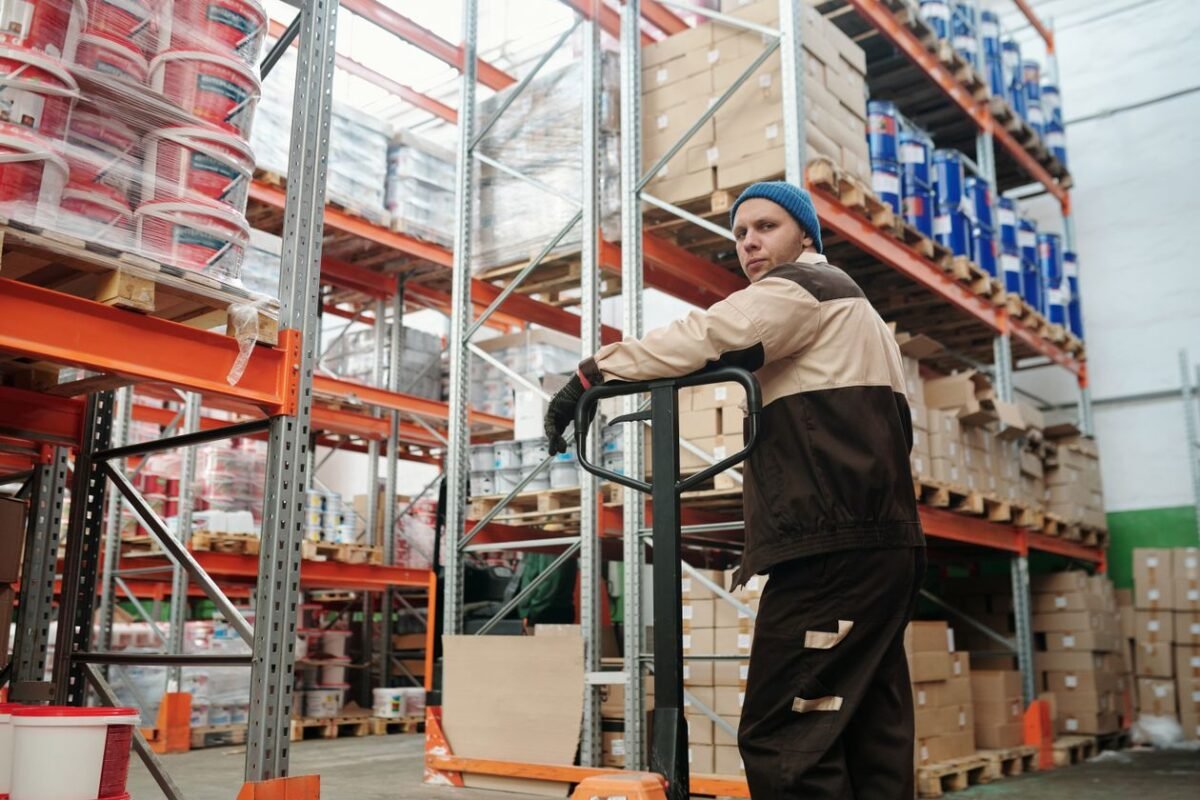Warehouse worker with a hand pallet jack beside pallet racking