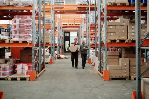 Two warehouse staff walking through a racked aisle with cartons
