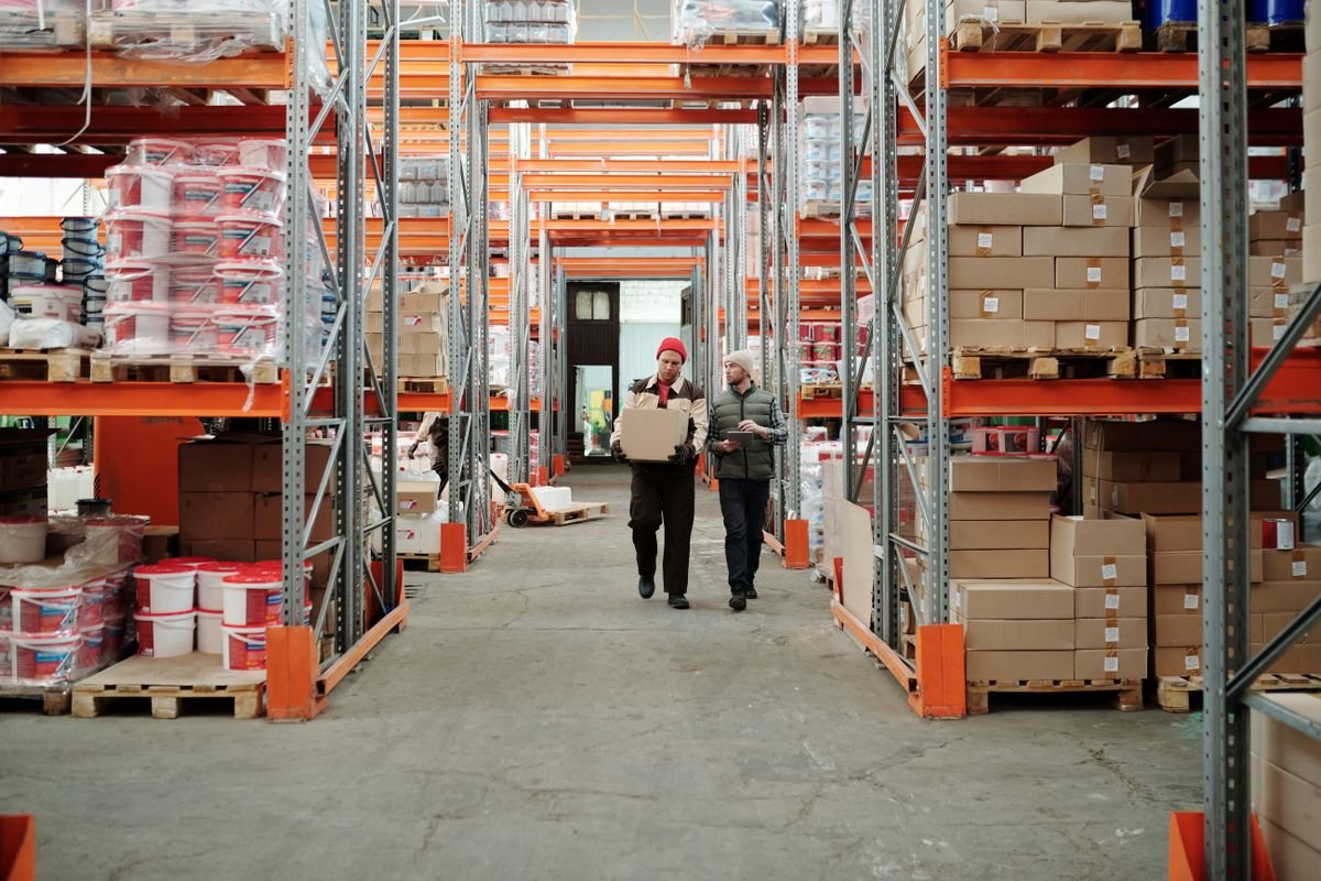 Two warehouse staff walking through a racked aisle with cartons