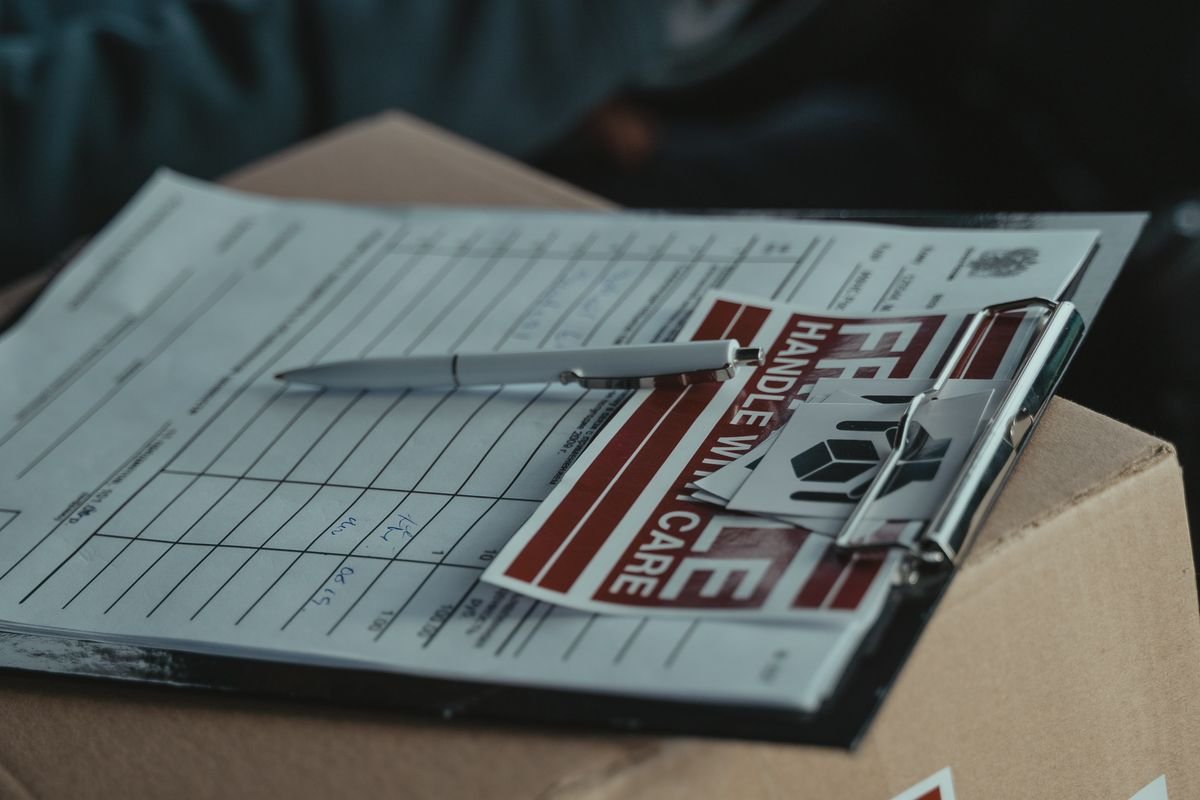 Clipboard with delivery paperwork resting on a cardboard carton