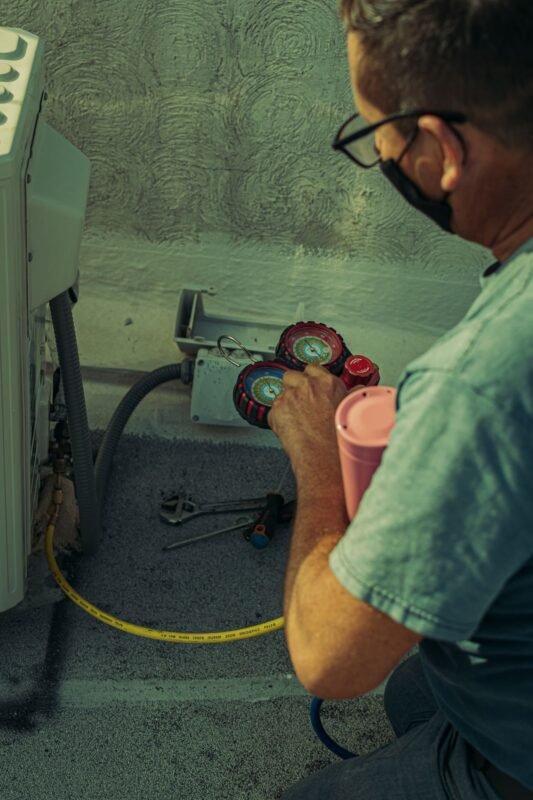 Technician checking refrigerant pressures with manifold gauges at a condensing unit