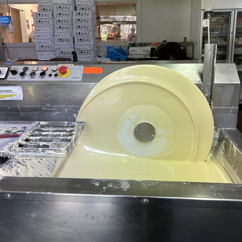 Stainless steel chocolate tempering wheel machine holding melted white chocolate in a small chocolate workshop