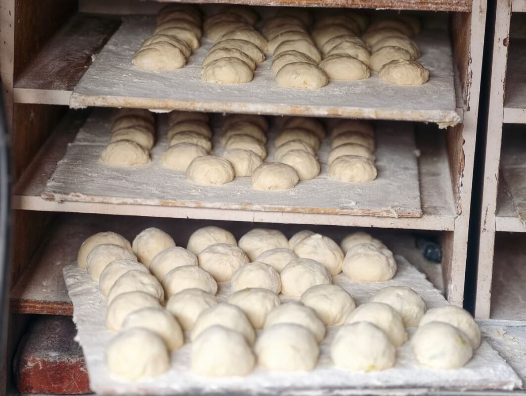 Yeast-raised bread dough balls proofing on floured trays in a bakery