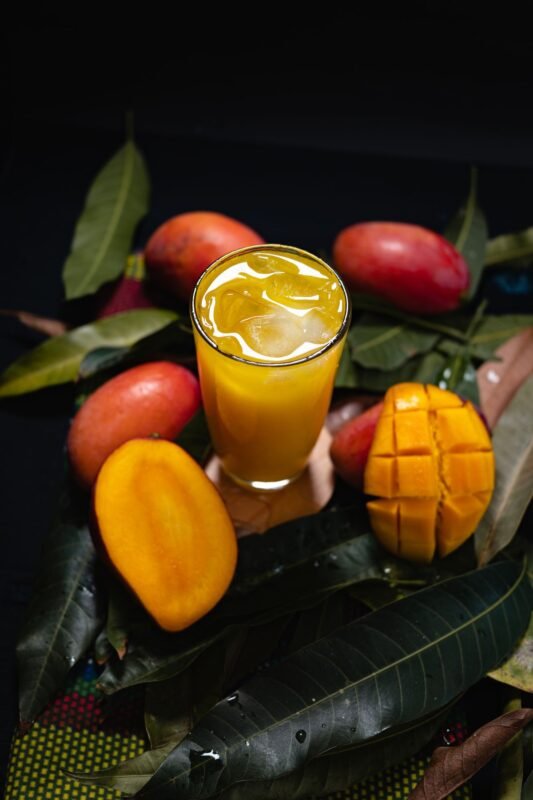 Glass of chilled mango juice surrounded by fresh ripe mangoes