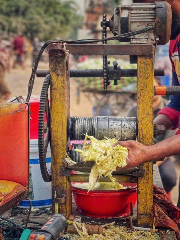 Vendor feeding sugarcane through an old motor-driven roller juice machine at a street stall