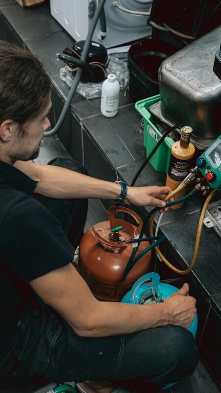 Technician connecting manifold gauges and a refrigerant cylinder for leak testing