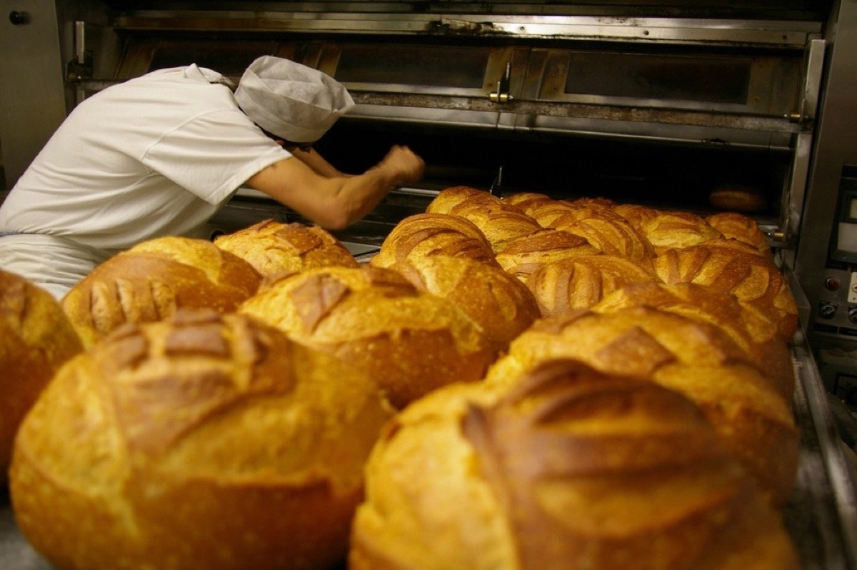 Baker taking fresh bread loaves out of a deck oven