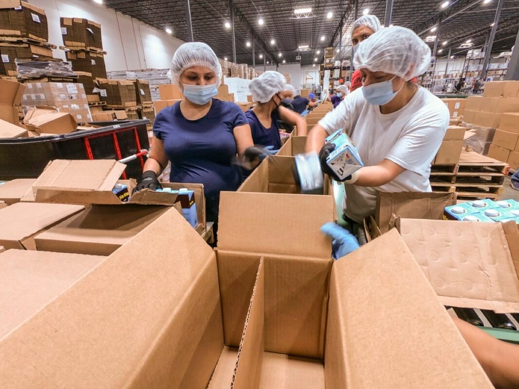 Workers in hairnets packing goods into cartons in a warehouse